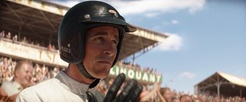 Movie still from “Ford v Ferrari” (2019), directed by James Mangold – A baseball player wearing a helmet and holding a baseball bat in front of a crowd of people; Close Up shot, Low angle