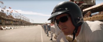 Movie still from “Ford v Ferrari” (2019), directed by James Mangold – A group of people lined up on the side of the road; Close Up shot, Over the shoulder angle