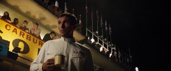 Movie still from “Ford v Ferrari” (2019), directed by James Mangold – A man holding a cup standing in front of a crowd; Medium shot, Low angle