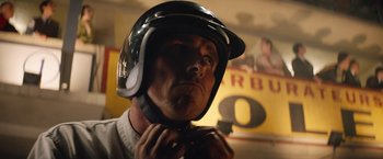 Movie still from “Ford v Ferrari” (2019), directed by James Mangold – A man wearing a motorcycle helmet while putting on a helmet; Close Up shot, Low angle