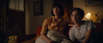 Movie still from “Ford v Ferrari” (2019), directed by James Mangold – A woman sitting on a couch next to a boy; Medium shot, Low angle