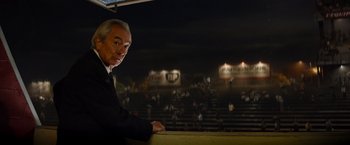Movie still from “Ford v Ferrari” (2019), directed by James Mangold – A man in a suit and tie standing in front of an audience; Medium shot, Low angle