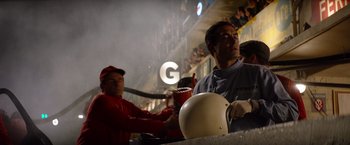 Movie still from “Ford v Ferrari” (2019), directed by James Mangold – A man holding a helmet in front of a crowd; Medium shot, Over the shoulder angle