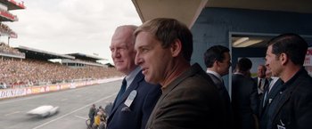 Movie still from “Ford v Ferrari” (2019), directed by James Mangold – Two men in suits are standing next to each other in a stadium; Close Up shot, Over the shoulder angle