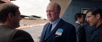 Movie still from “Ford v Ferrari” (2019), directed by James Mangold – An older man wearing a suit and tie; Close Up shot, Over the shoulder angle