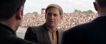 Movie still from “Ford v Ferrari” (2019), directed by James Mangold – A person wearing a suit near a crowd; Close Up shot, Over the shoulder angle