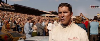 Movie still from “Ford v Ferrari” (2019), directed by James Mangold – A man standing in front of a group of people; Close Up shot, Over the shoulder angle