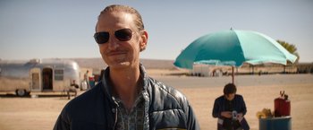 Movie still from “Ford v Ferrari” (2019), directed by James Mangold – A man with sunglasses and a blue umbrella in the background; Close Up shot, Over the shoulder angle