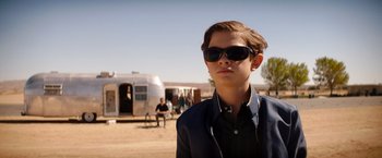 Movie still from “Ford v Ferrari” (2019), directed by James Mangold – A young man wearing sunglasses in front of an airstream trailer; Medium shot, Low angle