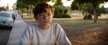 Movie still from “Ford v Ferrari” (2019), directed by James Mangold – A young boy sitting in the dirt near a tree; Close Up shot, Over the shoulder angle