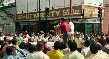 Movie still from “Detroit” (2017), directed by Kathryn Bigelow – A crowd of people standing around a street corner; Extreme Wide shot, High angle
