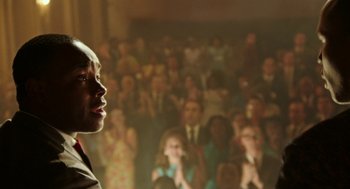 Movie still from “Detroit” (2017), directed by Kathryn Bigelow – A man standing in front of a crowd of onlookers; Close Up shot, Over the shoulder angle