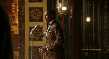 Movie still from “Detroit” (2017), directed by Kathryn Bigelow – A man wearing a suit standing at a microphone; Medium shot, Over the shoulder angle