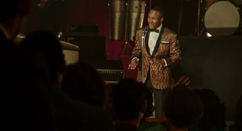 Movie still from “Detroit” (2017), directed by Kathryn Bigelow – A man wearing a suit and bow tie talking to a group of people; Medium shot, Over the shoulder angle