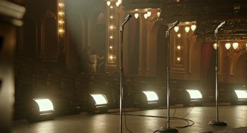 Movie still from “Detroit” (2017), directed by Kathryn Bigelow – Two microphones are set up in front of a stage with lights; Wide shot, High angle