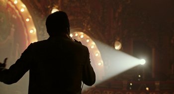 Movie still from “Detroit” (2017), directed by Kathryn Bigelow – A man standing on a stage in front of a microphone; Medium shot, Low angle