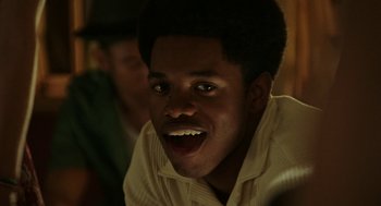 Movie still from “Detroit” (2017), directed by Kathryn Bigelow – A young man with dark hair and green eyes smiling for the camera; Close Up shot, Over the shoulder angle