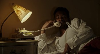 Movie still from “Detroit” (2017), directed by Kathryn Bigelow – A man sitting in a bed talking on a phone; Medium shot, High angle