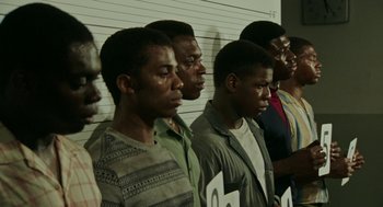 Movie still from “Detroit” (2017), directed by Kathryn Bigelow – A group of men standing next to each other in front of a wall; Medium shot, High angle