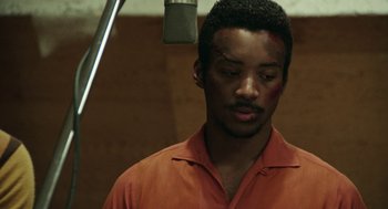 Movie still from “Detroit” (2017), directed by Kathryn Bigelow – A man in an orange shirt is in front of a microphone; Close Up shot, Over the shoulder angle