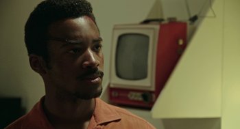 Movie still from “Detroit” (2017), directed by Kathryn Bigelow – A black man with a red television in the background; Close Up shot, Over the shoulder angle