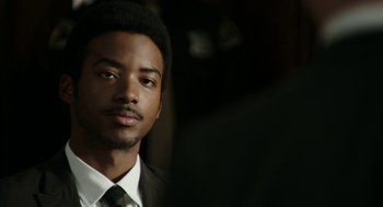 Movie still from “Detroit” (2017), directed by Kathryn Bigelow – A man in a suit and tie looking at the camera; Close Up shot, Over the shoulder angle