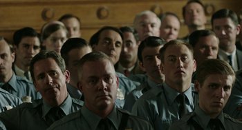 Movie still from “Detroit” (2017), directed by Kathryn Bigelow – A large group of men in police uniforms in front of a wooden wall; Medium shot, High angle