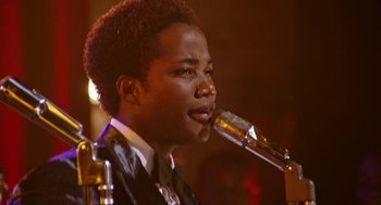 Movie still from “Detroit” (2017), directed by Kathryn Bigelow – A man in a suit is singing into a microphone; Close Up shot, Over the shoulder angle