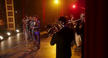 Movie still from “Detroit” (2017), directed by Kathryn Bigelow – A group of men in suits and ties playing musical instruments in front of microphones; Extreme Wide shot, Low angle