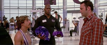 Movie still from “Dodgeball: A True Underdog Story” (2004), directed by Rawson Marshall Thurber – A man in a gym holding a pom - pom; Medium shot, Over the shoulder angle
