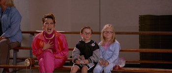 Movie still from “Dodgeball: A True Underdog Story” (2004), directed by Rawson Marshall Thurber – Three children sitting on a bench with a woman standing next to them; Medium shot, Over the shoulder angle