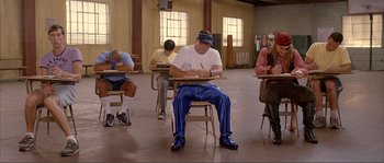Movie still from “Dodgeball: A True Underdog Story” (2004), directed by Rawson Marshall Thurber – A group of people sitting at a desk writing on papers; Wide shot, High angle