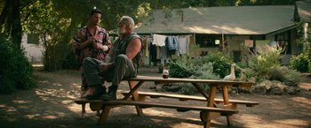 Movie still from “Dog” (2022), directed by Reid Carolin – A man sitting on top of a wooden bench next to another man; Wide shot, Over the shoulder angle