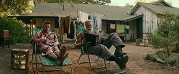 Movie still from “Dog” (2022), directed by Reid Carolin – An older man sitting in a lawn chair reading a book; Wide shot, Low angle