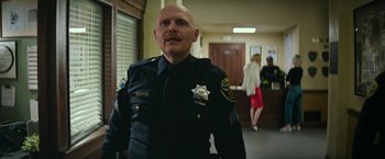 Movie still from “Dog” (2022), directed by Reid Carolin – A man in a police uniform standing next to a door way; Medium shot, Low angle