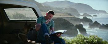Movie still from “Dog” (2022), directed by Reid Carolin – A man sitting in the back of a truck reading a book; Medium shot, Low angle