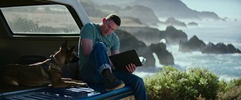 Movie still from “Dog” (2022), directed by Reid Carolin – A man sitting on the back of a truck with a laptop; Medium shot, High angle