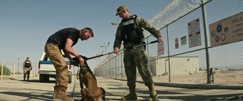 Movie still from “Dog” (2022), directed by Reid Carolin – Two men in military garb with a dog in a fenced area; Wide shot, Low angle
