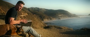 Movie still from “Dog” (2022), directed by Reid Carolin – A person sitting on a bench on the beach with chopsticks in their hands; Wide shot, Low angle