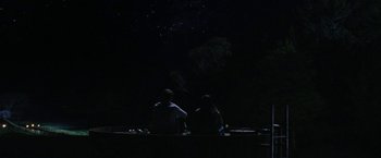 Movie still from “Don't Make Me Go” (2022), directed by Hannah Marks – Two people sitting on a bench in the dark; Extreme Wide shot, Overhead angle