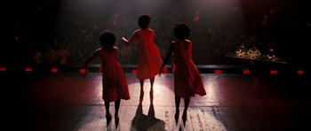 Movie still from “Dreamgirls” (2006), directed by Bill Condon – A group of women in red dresses on a stage; Wide shot, Low angle