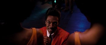 Movie still from “Dreamgirls” (2006), directed by Bill Condon – A man in a red suit is posing for a picture; Close Up shot, Over the shoulder angle
