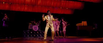 Movie still from “Dreamgirls” (2006), directed by Bill Condon – A man is singing on stage with a group of women; Wide shot, Low angle