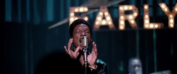 Movie still from “Dreamgirls” (2006), directed by Bill Condon – A man is singing into a microphone in front of a lit up eat sign; Close Up shot, Over the shoulder angle
