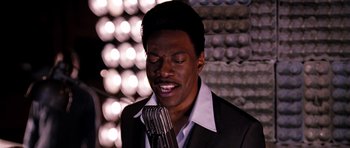 Movie still from “Dreamgirls” (2006), directed by Bill Condon – A man in a black suit is singing into a microphone; Close Up shot, High angle