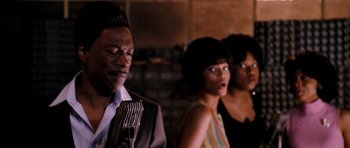 Movie still from “Dreamgirls” (2006), directed by Bill Condon – A man and two women singing in front of a brick wall; Close Up shot, Over the shoulder angle