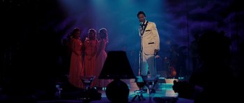 Movie still from “Dreamgirls” (2006), directed by Bill Condon – A man in a white suit is on a stage; Wide shot, Low angle