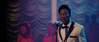 Movie still from “Dreamgirls” (2006), directed by Bill Condon – A man standing in front of a microphone in front of a group of people; Close Up shot, Over the shoulder angle