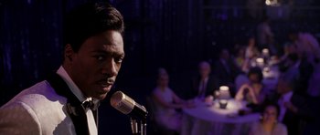 Movie still from “Dreamgirls” (2006), directed by Bill Condon – A man standing in front of a microphone in front of a group of people; Close Up shot, Over the shoulder angle