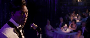 Movie still from “Dreamgirls” (2006), directed by Bill Condon – A man standing at a microphone in front of a table; Close Up shot, Over the shoulder angle